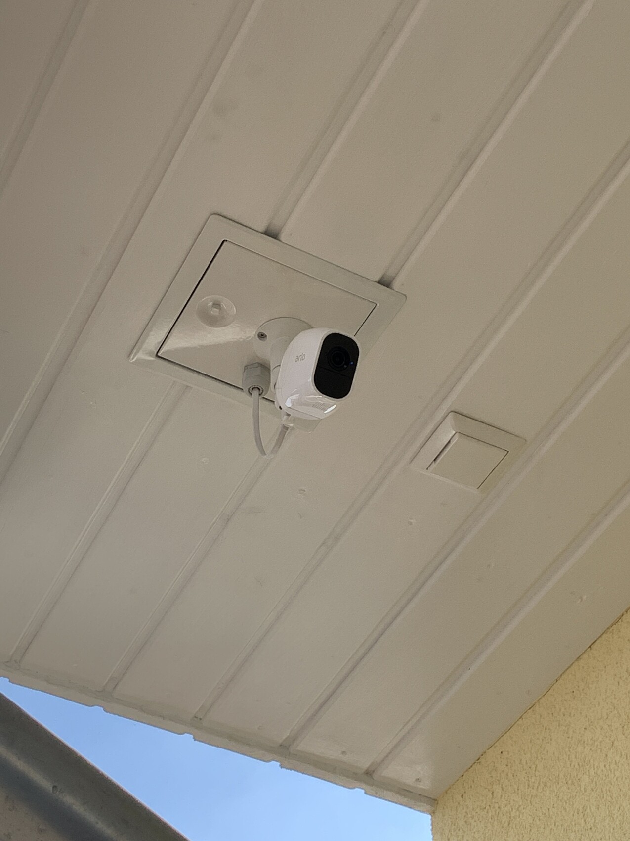 Weiße Überwachungskamera an einer weißen Paneeldecke, von unten gesehen.