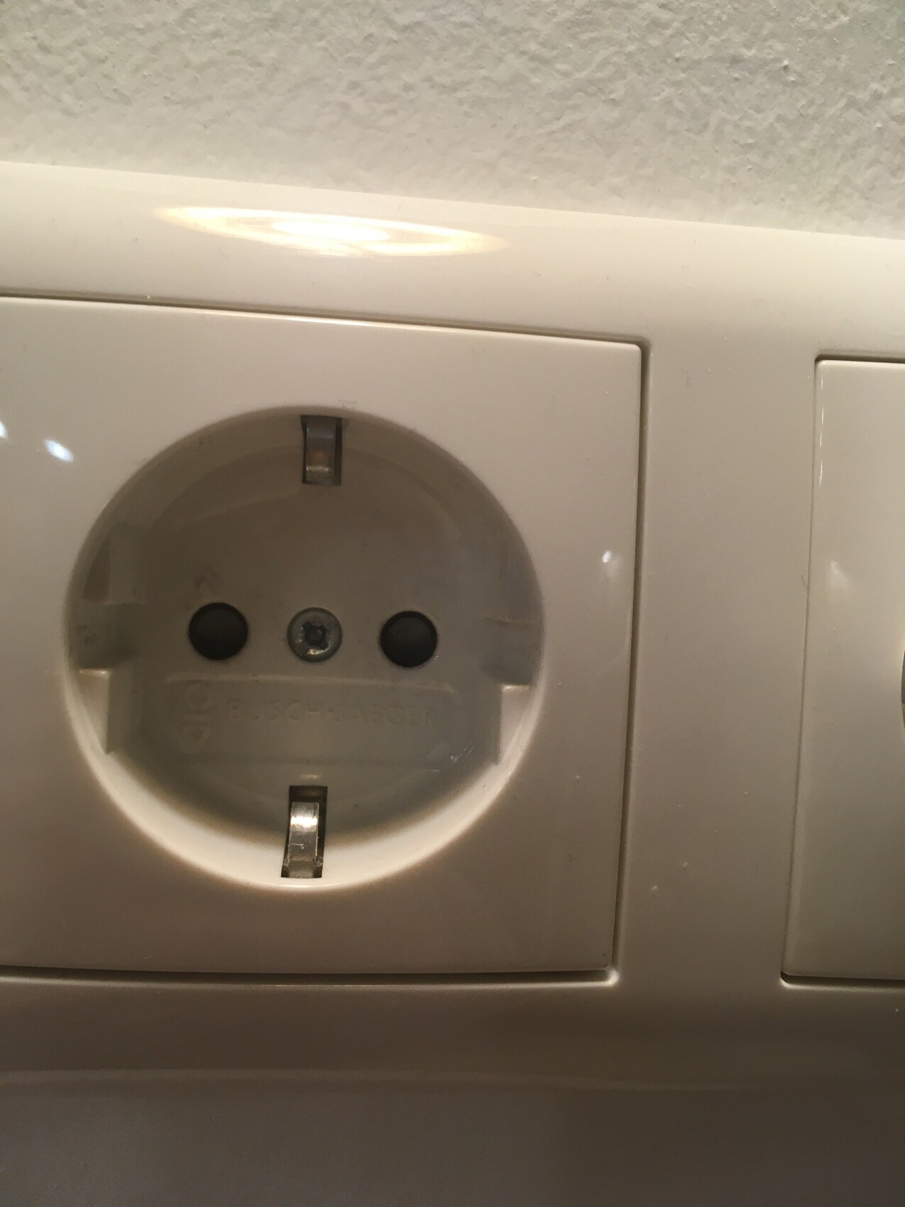 Weiße Schuko-Steckdose in Wandplatte mit zwei runden Löchern, daneben Lichtschalter.