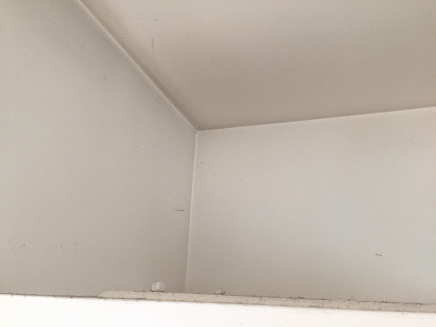 Weiße Innenraum-Ecke aus zwei Wänden und Decke, leicht staubig.
