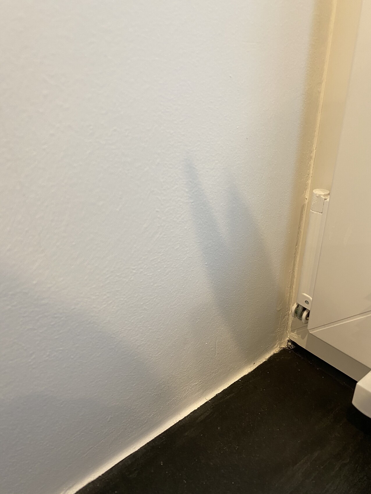 Eckansicht: weiße Wand, dunkler Boden, Sockelleiste; rechts ein weißes Möbelseitenteil.