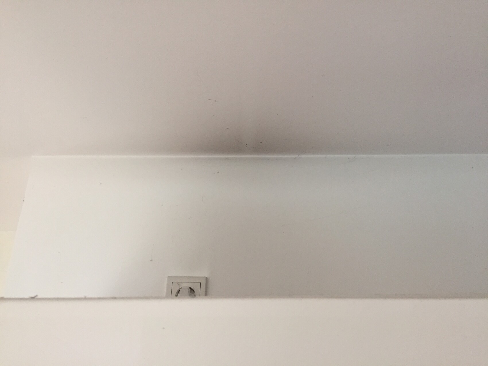 Weisse Innenwand mit Ablagekante und sichtbarer Steckdose am unteren Rand
