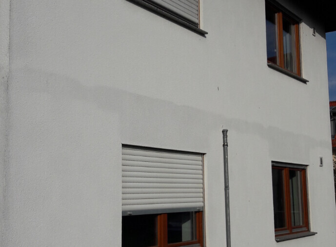 Außenansicht eines Hauses mit weißer Fassade, Holzfenstern und Rollläden