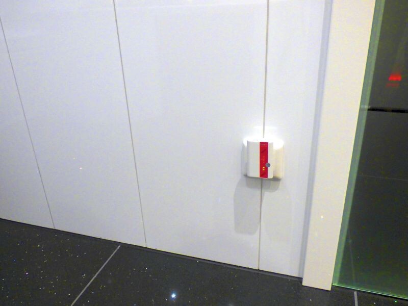 Weiße Wandpaneele mit kleinem weißen Lichtschalter und rotem Streifen, dunkler Boden, Glasseite.