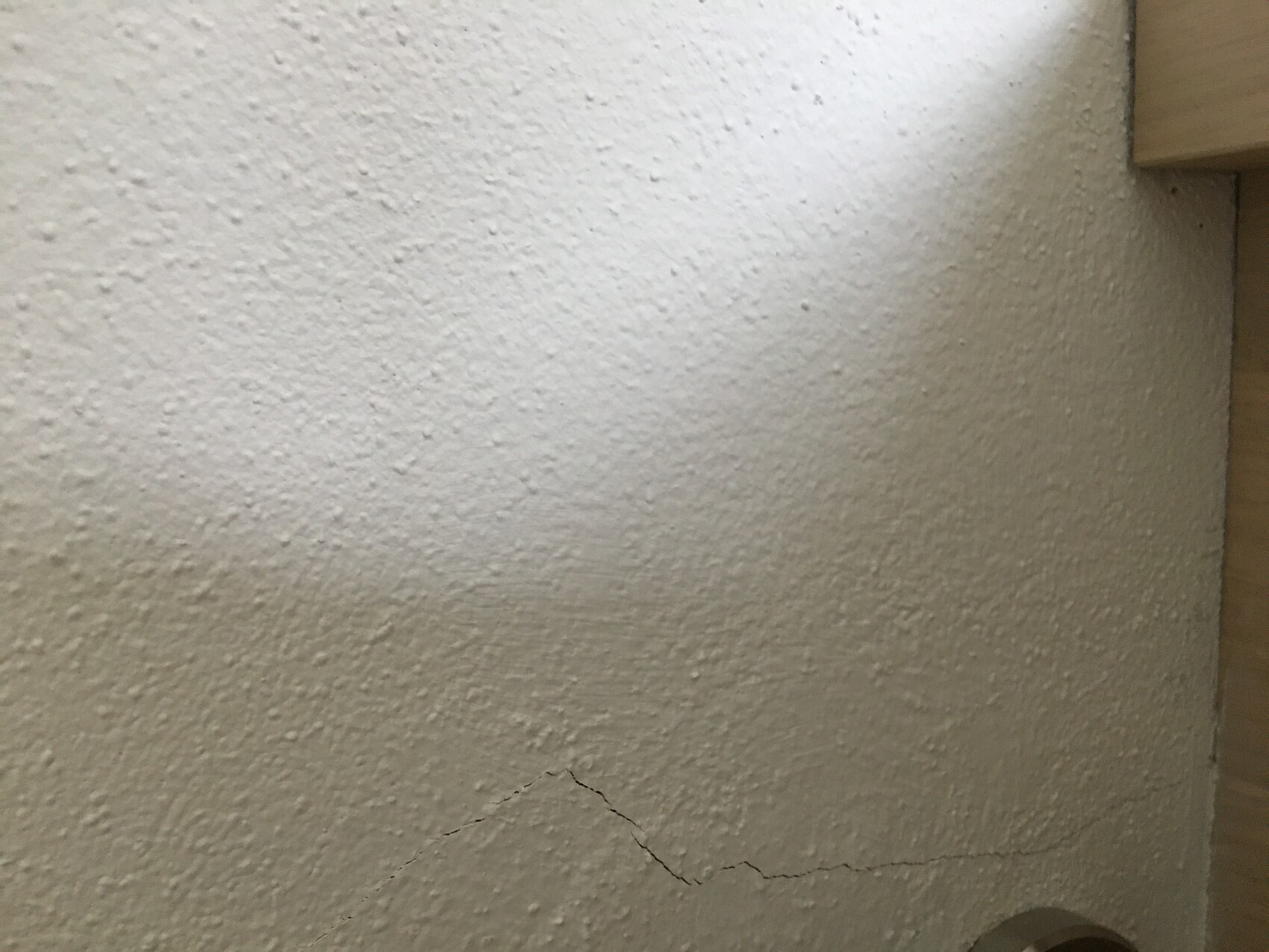 Weiße Wand mit grober Putzstruktur; unten sichtbarer Riss, rechts oben Holzverkleidung.