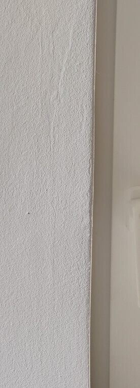Weiße, leicht strukturierte Wand links neben einer senkrechten Türkante rechts