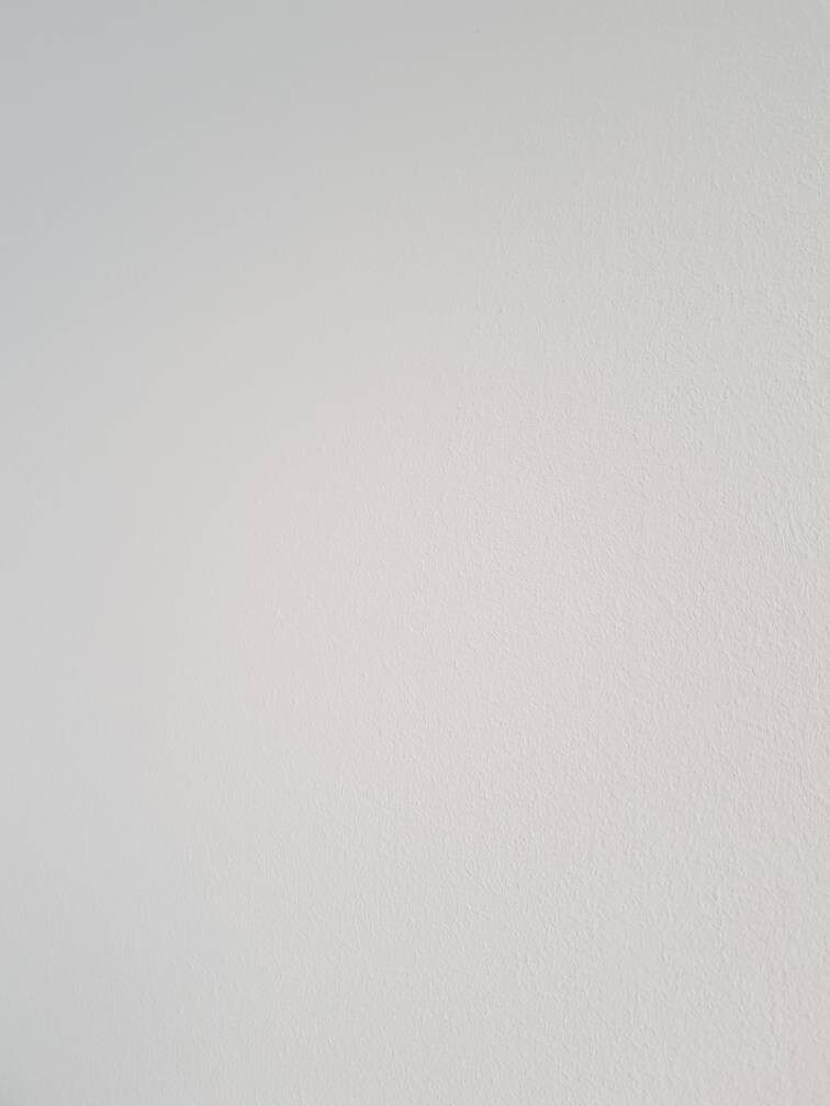 Weiße Wand mit feiner Struktur und leichter Schattierung.