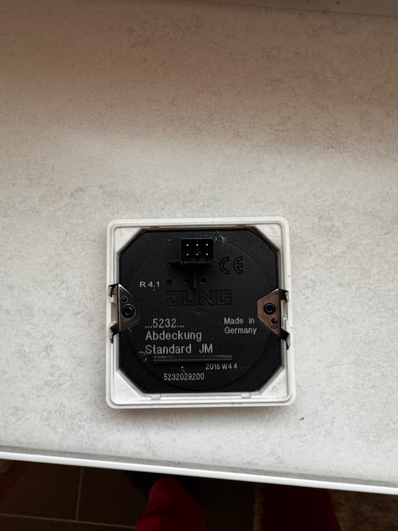 Weisse quadratische Wandabdeckung mit schwarzer runder Elektro-Dose, Marke JUNG