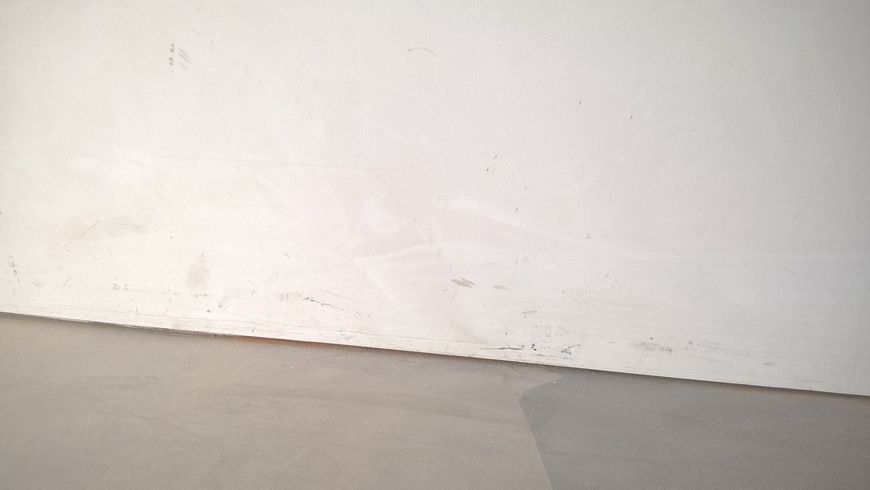 Weiße Wand mit Kratzern und Schmierflecken am unteren Rand, grauer Boden.