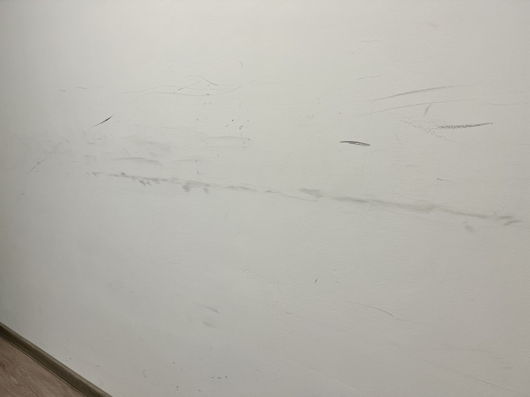 Weiße Wand mit sichtbaren Kratzern und Schrammen; Sockelleiste am unteren Rand.