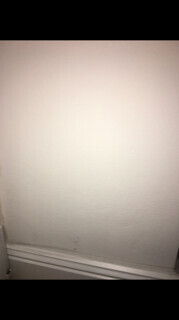 Eine weiße Innenwand mit Sockelleiste und leichten Verschmutzungen in der unteren Ecke.