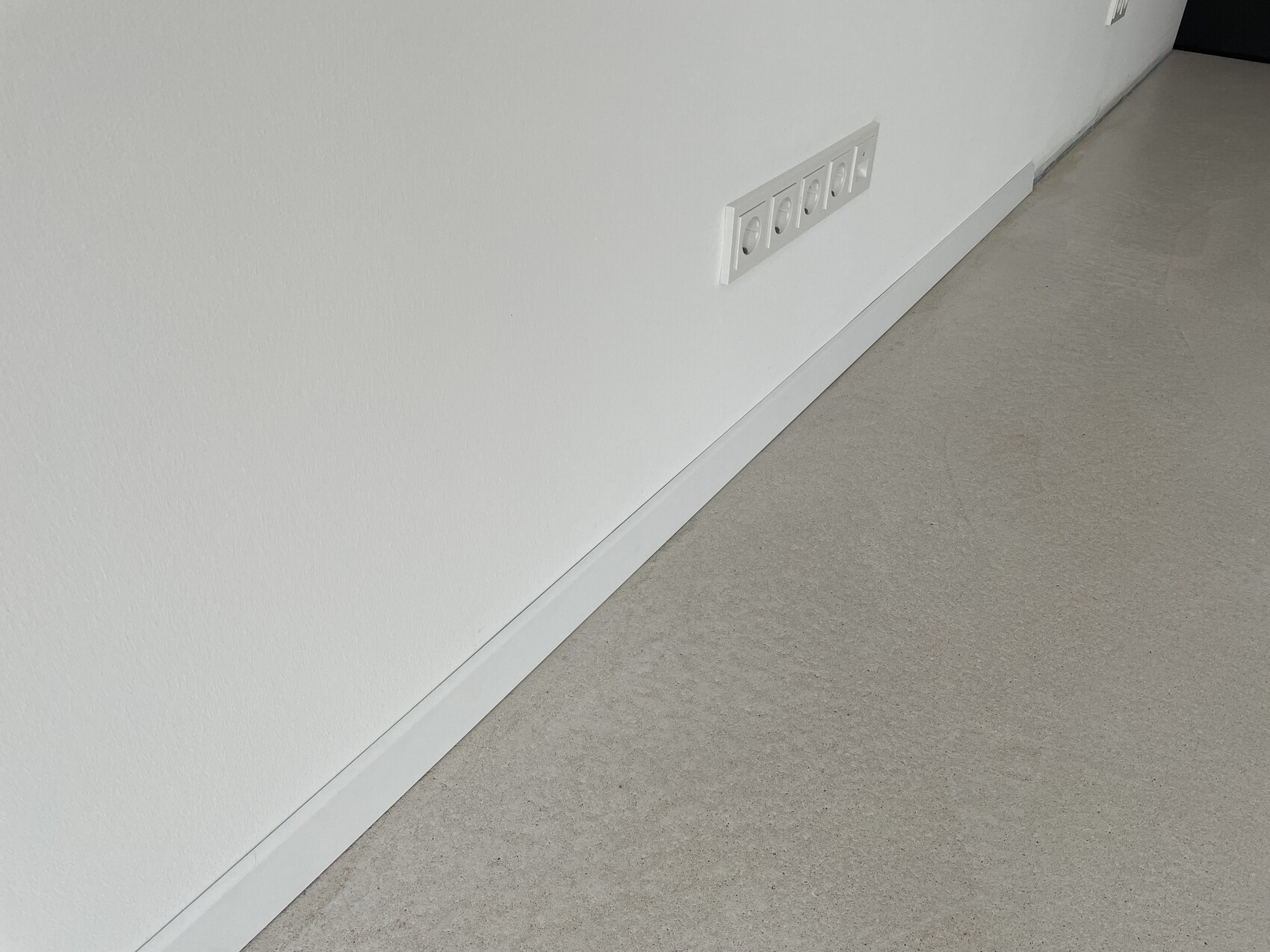 Weiße Wand mit sechs Schuko-Steckdosen in einer Wandplatte über der Bodenleiste.