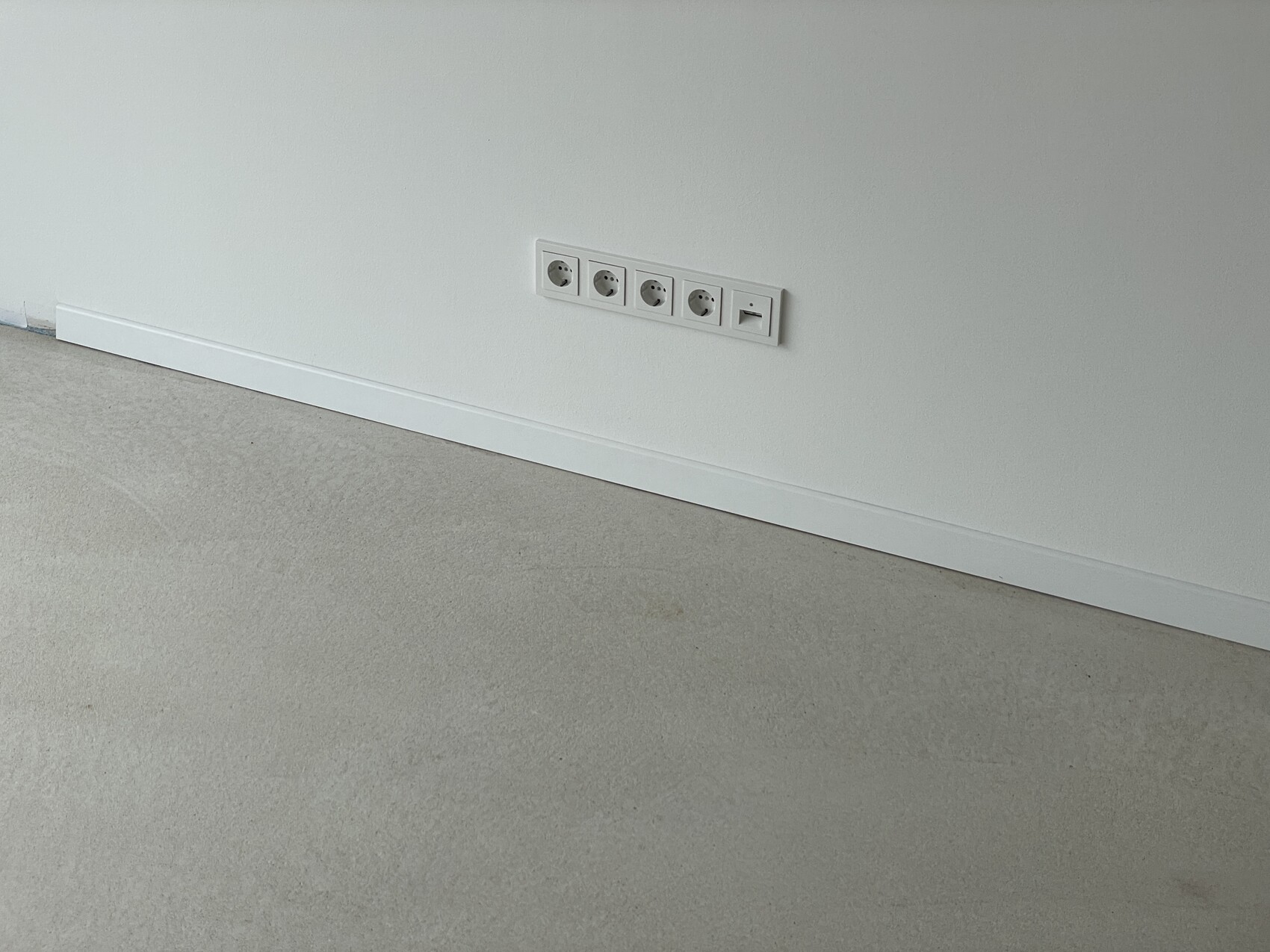 Weiße Wand mit Reihe runder Steckdosen nahe Fußleiste über hellgrauen Teppichboden.