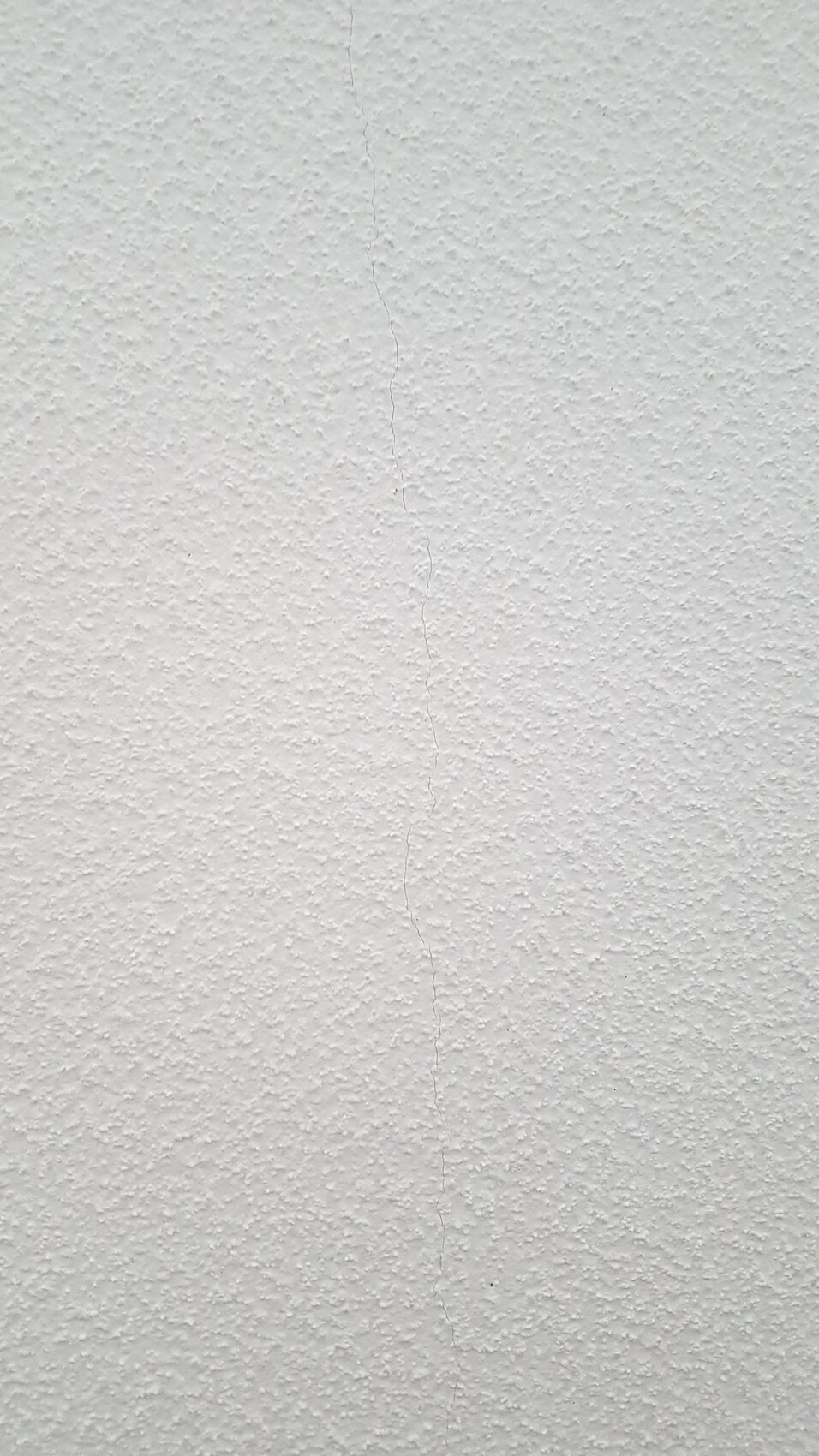 Weiße strukturierte Wand mit sichtbar vertikalem Riss.
