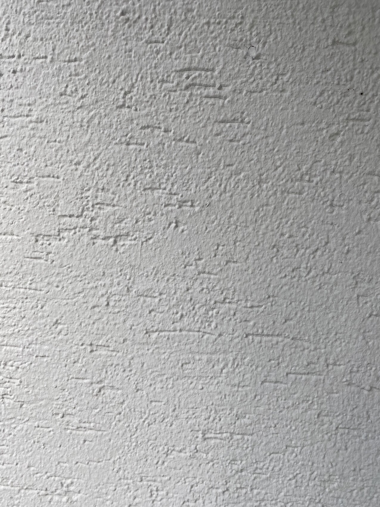 Grobe, weiße Wandoberfläche mit unregelmäßigem Putzrelief.