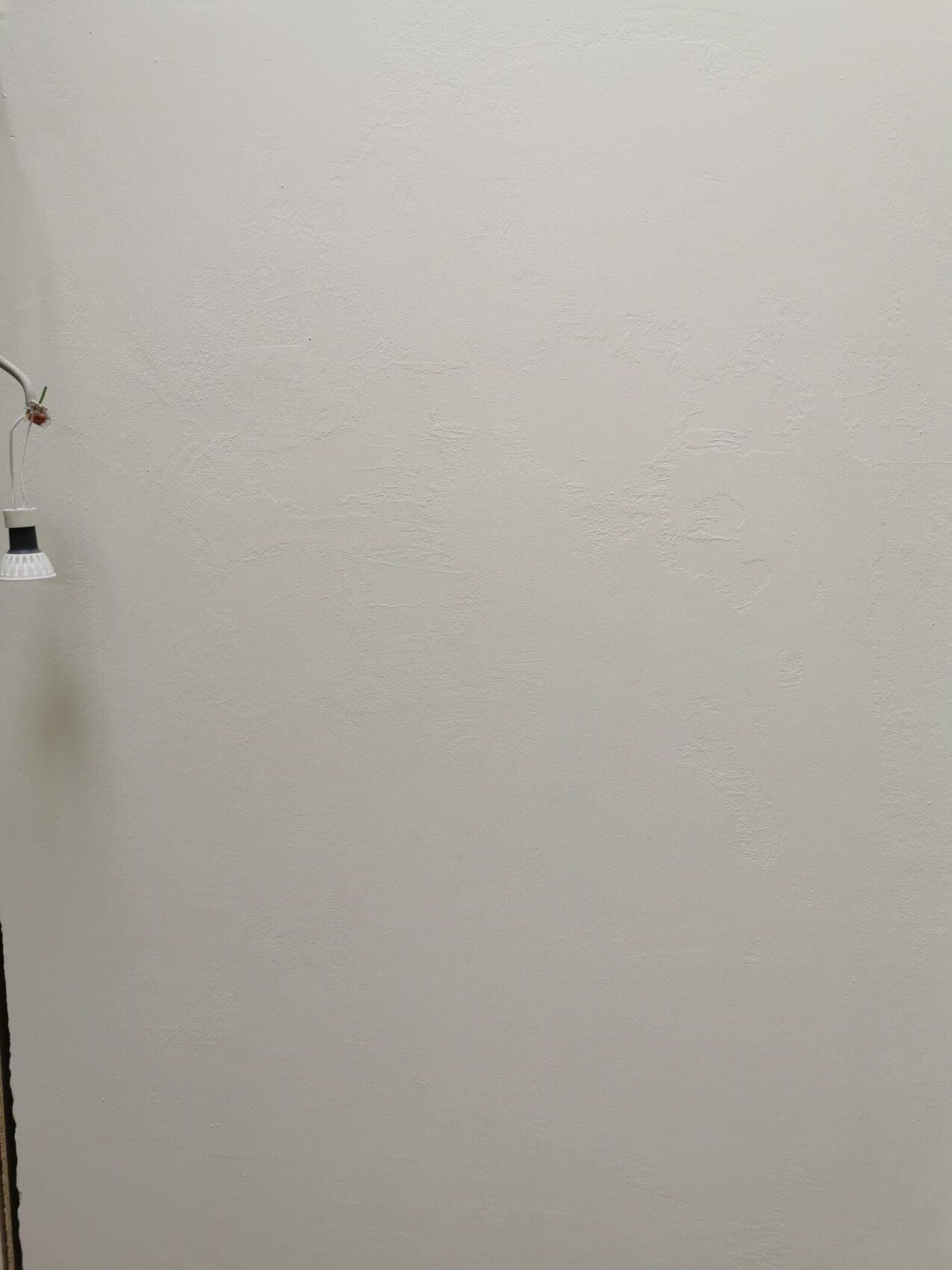 Schlichte texturierte weiße Wand mit einer hängenden Lampe links und sichtbaren Kabeln.