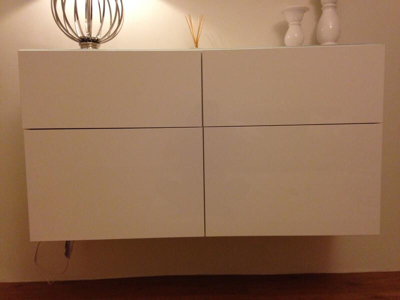 Weiße wandmontierte Wohnzimmerschrank mit Dekorationen und warmer Beleuchtung.