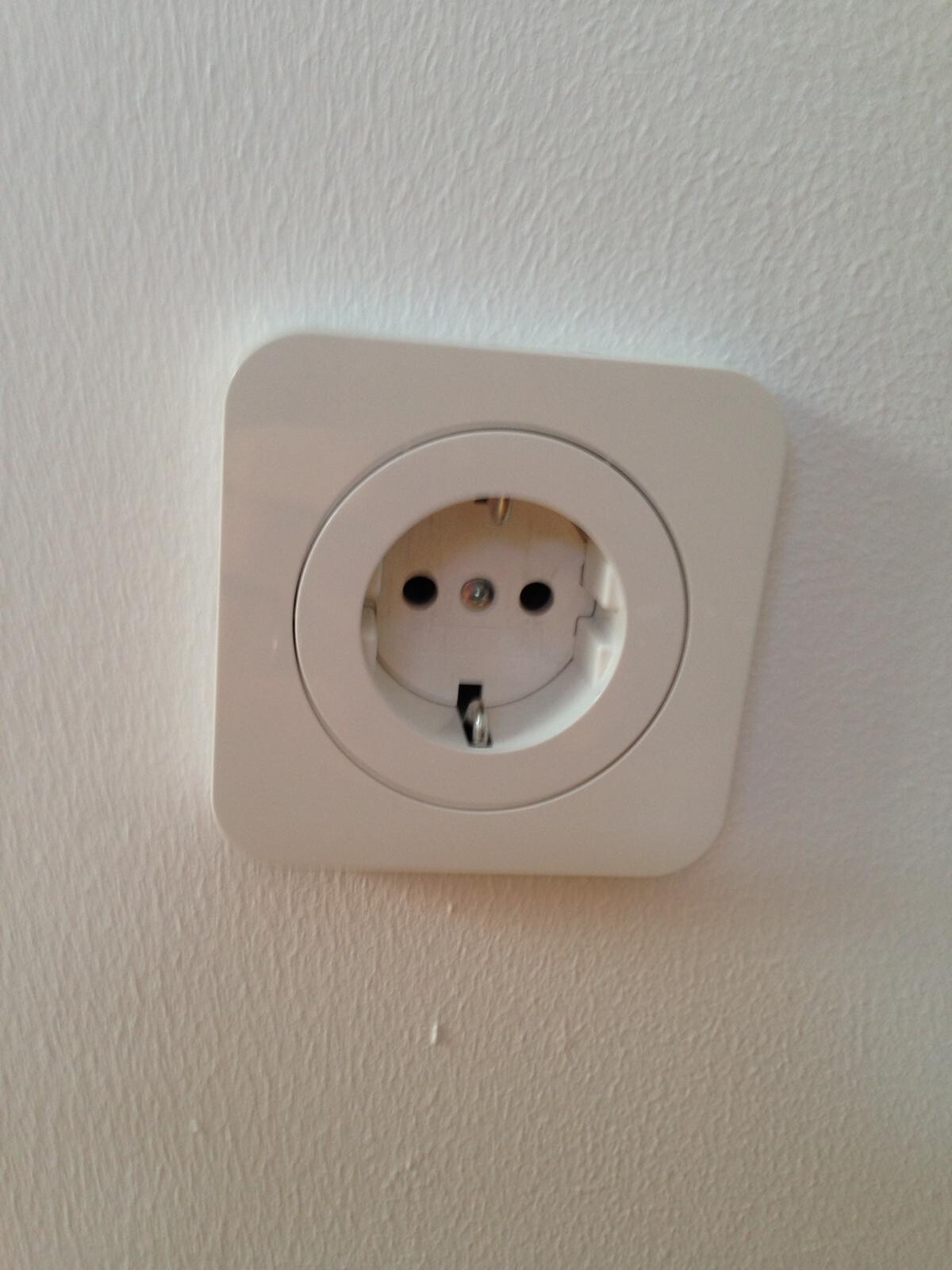 Weisse Wandsteckdose in Wandmontage, runde Form, zwei Steckdosenlöcher.