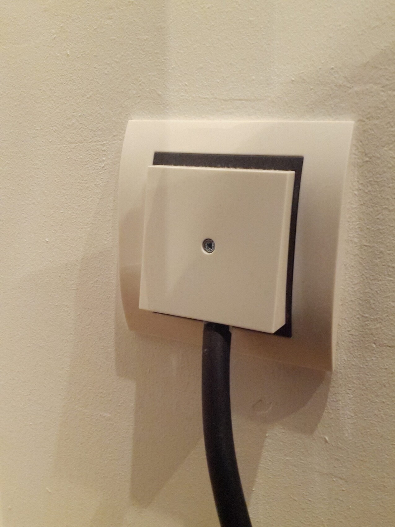Weiße quadratische Wandsteckdose mit schwarzem Kabel an heller Wand