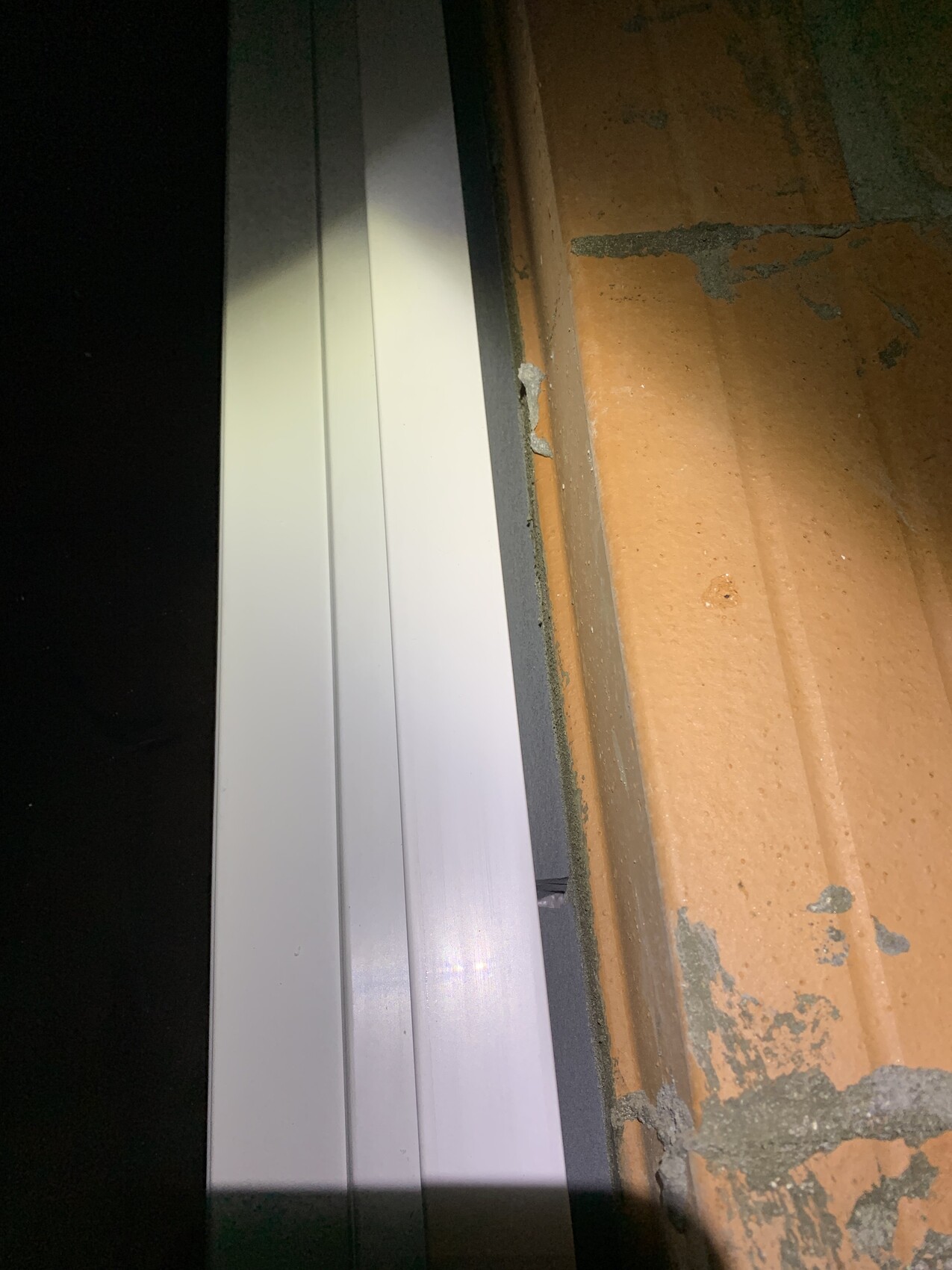 Nahaufnahme eines weißen Fensterrahmens an einer unverputzten Backsteinwand mit Mörtelresten.