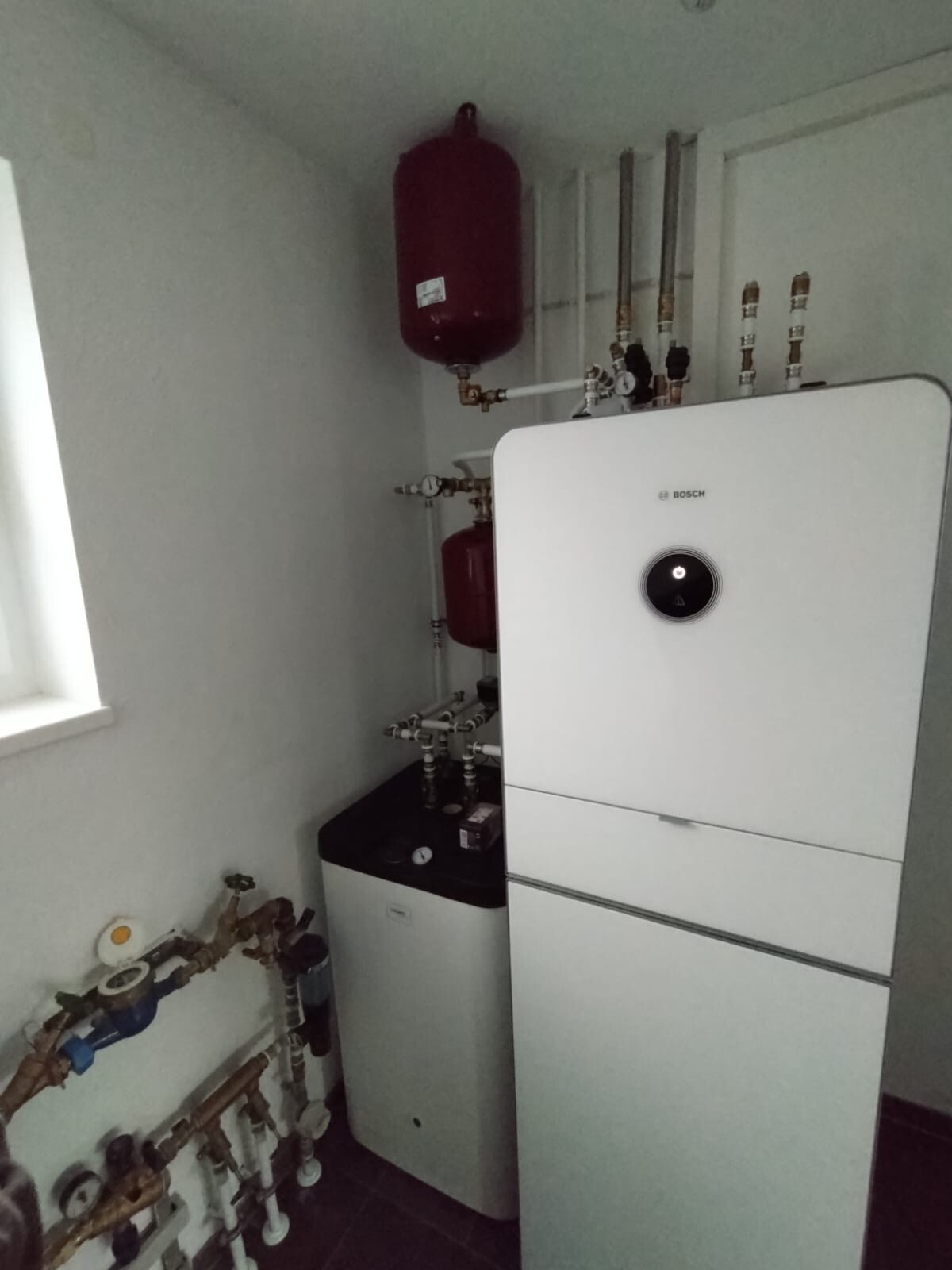 Bosch Heizungsanlage mit Warmwasserspeicher, roter Ausdehnungsbehälter und Rohrleitungen