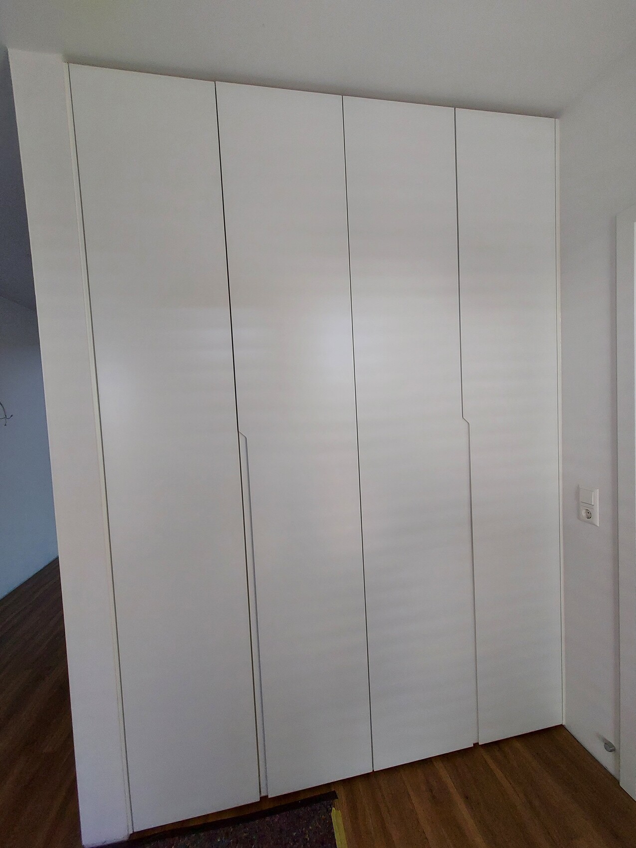 Weißer, mehrteiliger Kleiderschrank mit vier Türen auf Holzfußboden.