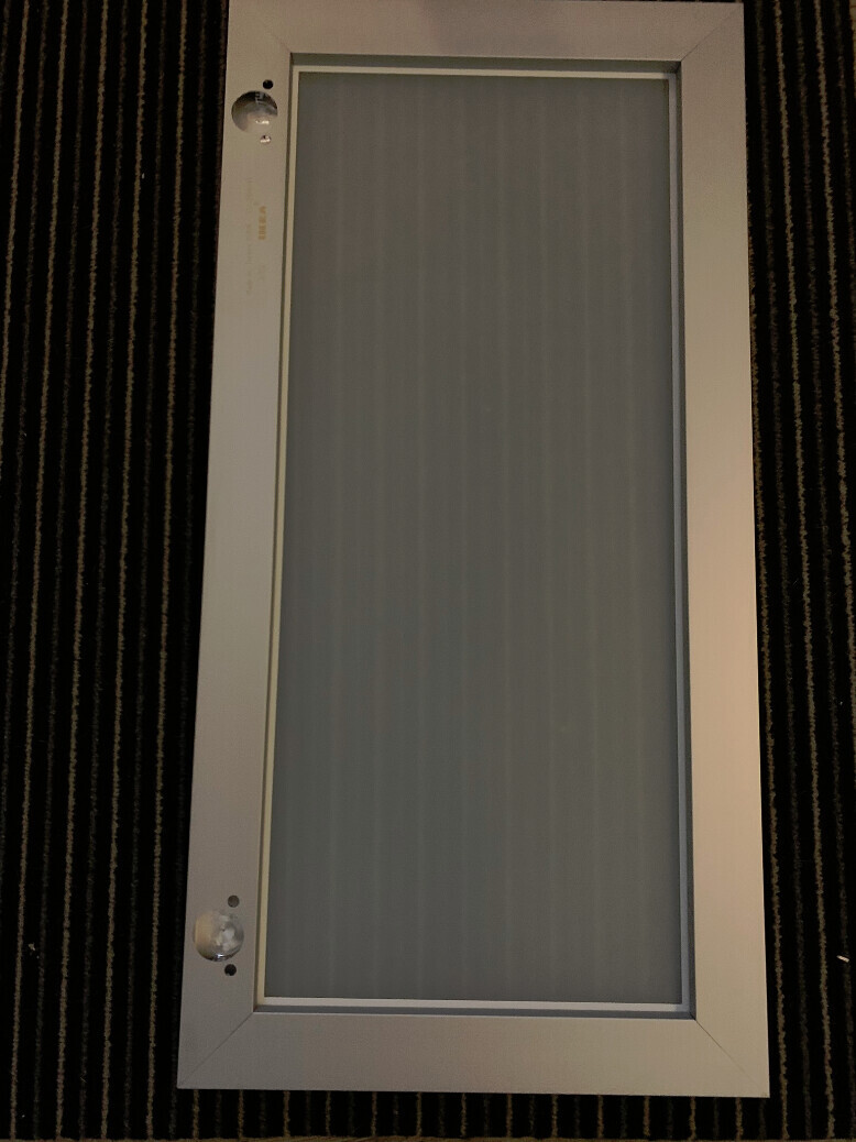 Vertikales Frostglasfenster mit weißem Rahmen auf dunkel gestreiftem Teppichboden.