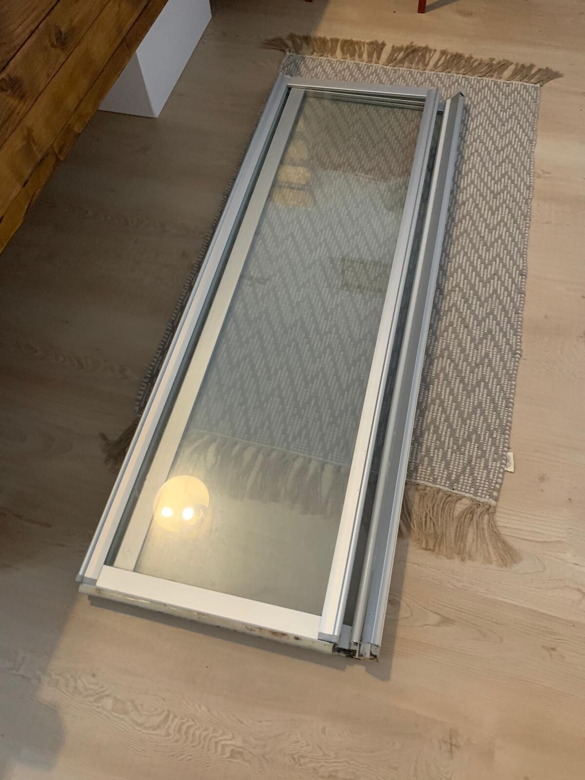 Weißer Fensterrahmen mit Glas liegt flach auf Holzboden neben Teppich.