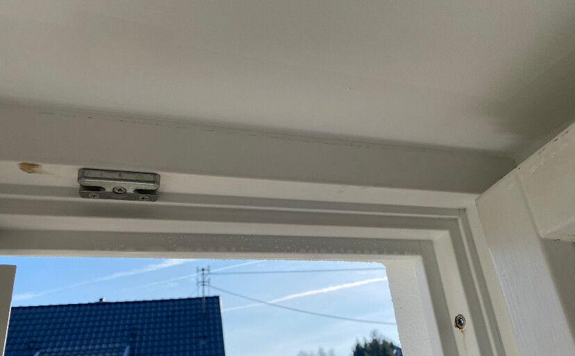 Weißer Innenfensterrahmen; offenes Fenster mit Blick auf blauen Himmel, blaues Dach und Kabel.