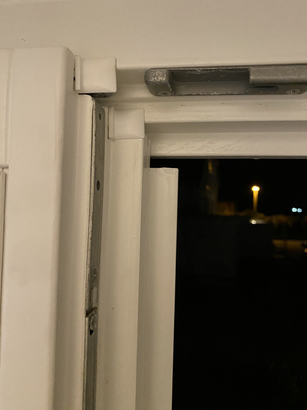 Nahaufnahme eines weißen Fensterrahmens mit Scharnier; Blick nach draußen bei Nacht.
