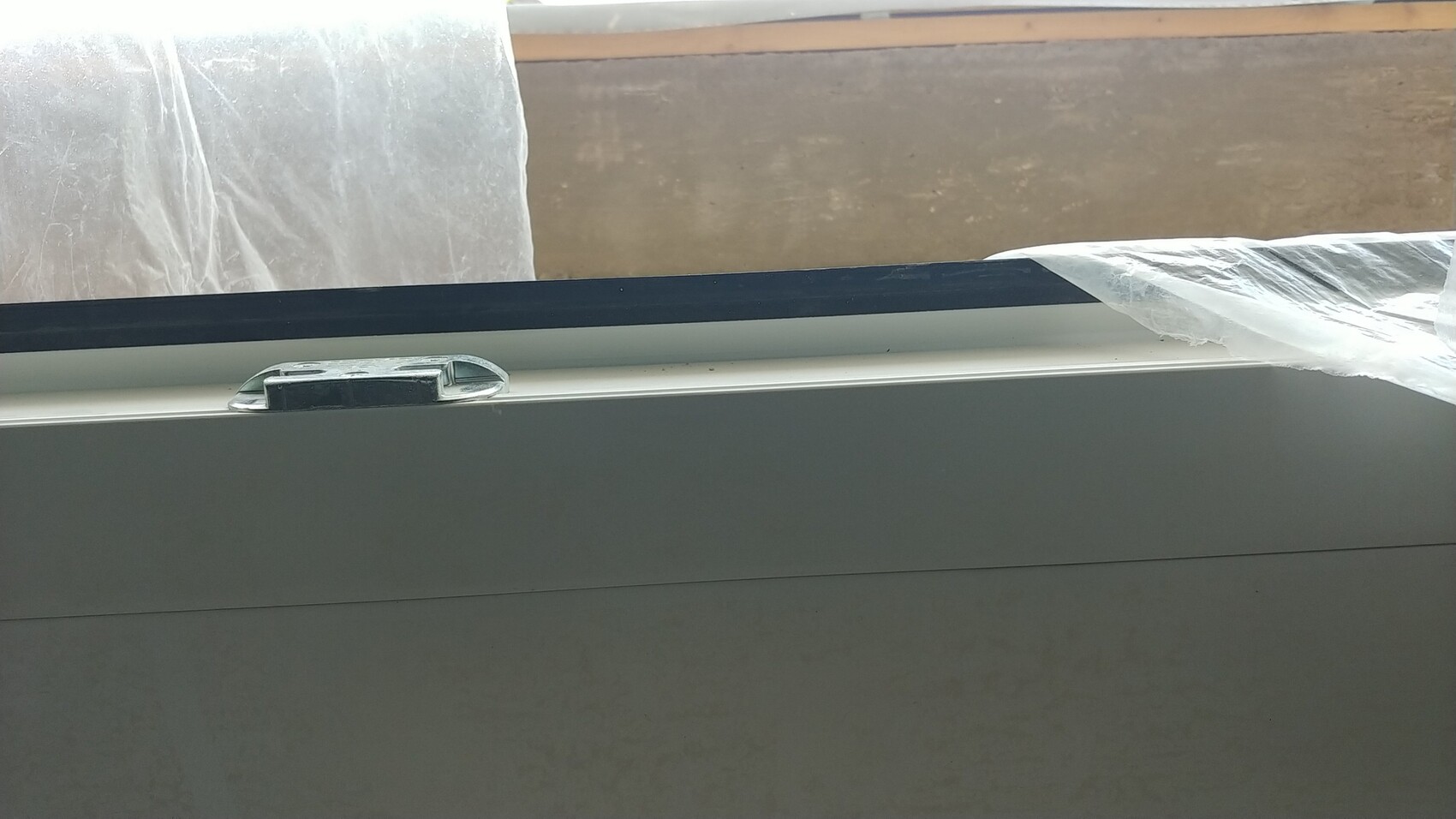 Weißer Fensterrahmen mit Griff und Schutzfolie, Bauumgebung sichtbar.