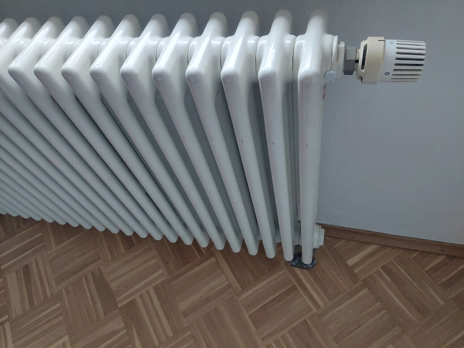 Weißer Heizkörper mit Thermostatventil an der Wand, auf Holzfußboden.