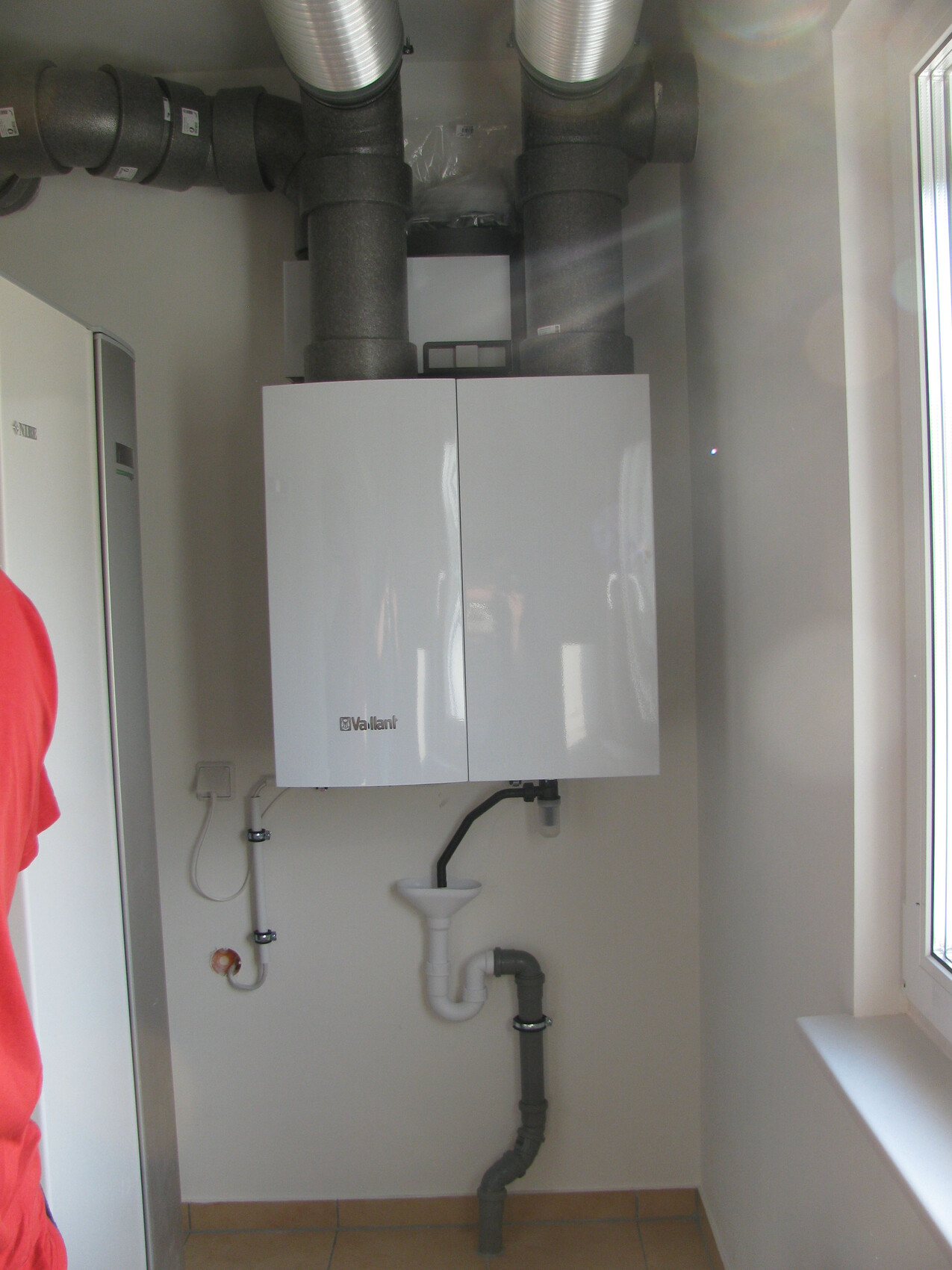 Vaillant-Wandheizgerät an der Wand, sichtbare Abgasleitungen und Rohrleitungen darunter.