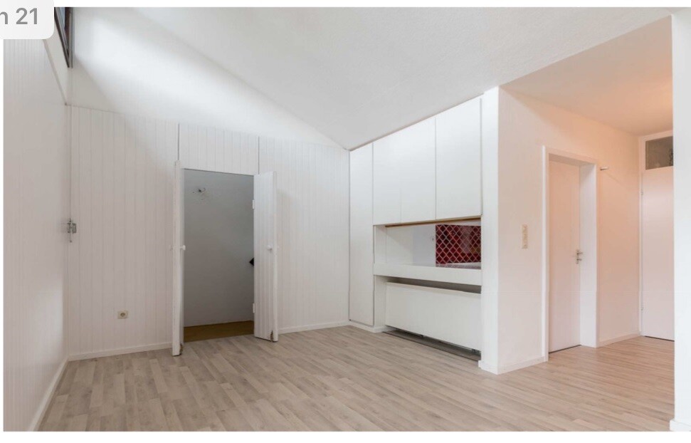 Heller, leerer Raum mit weißen Einbauschränken, Holzboden, schräger Decke und offenem Türdurchgang.