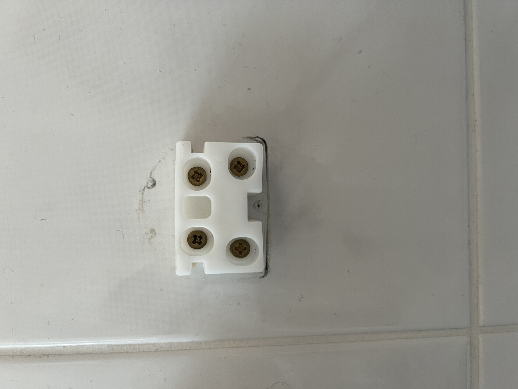 Weißer Terminalblock mit vier Schrauben an Fliesenwand