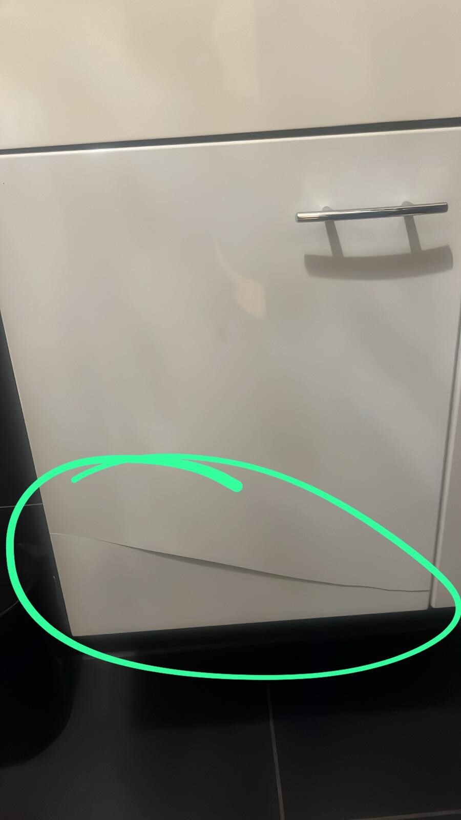 Weiße Küchenfront oder Geräteschrank mit Griff; untere Kante zeigt Riss.