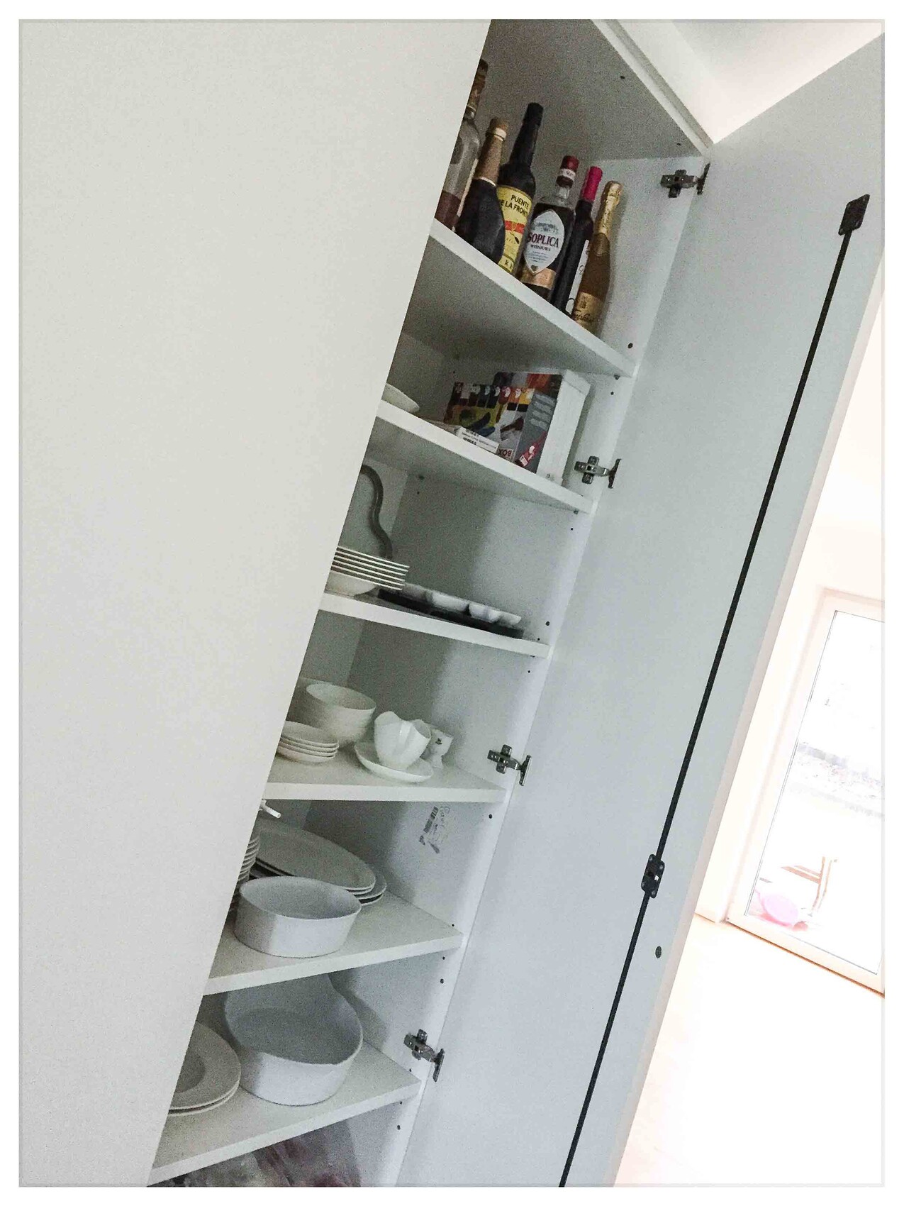 Offener weisser Kuechenschrank mit Geschirr, Tassen und Flaschen in einer Küche