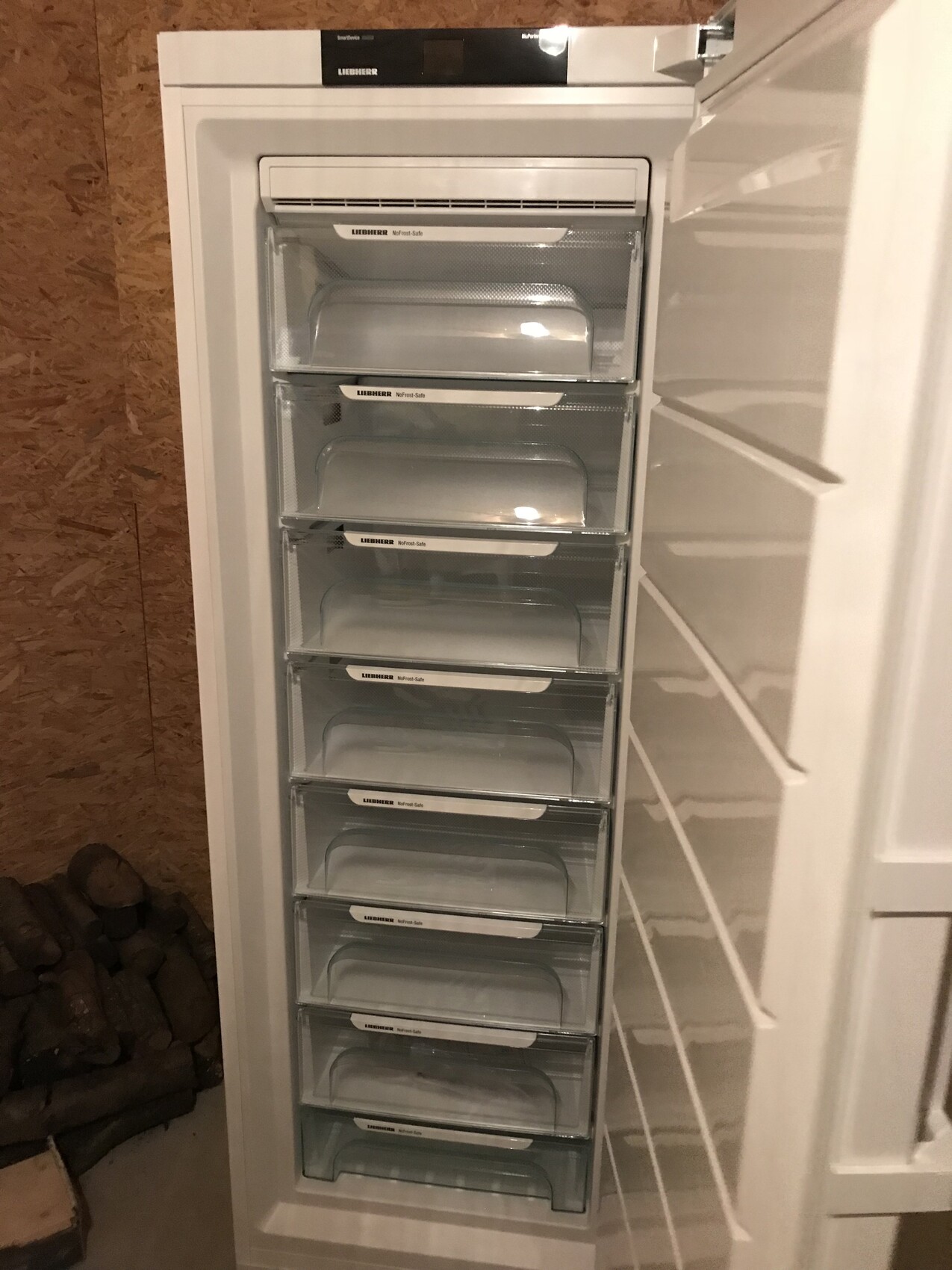 Offener Gefrierschrank mit mehreren transparenten Schubladen in einer Holzwand-Nische.