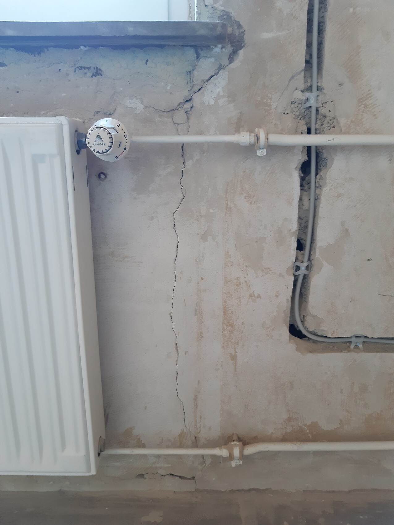 Weißer Heizkörper links, Rohre verlaufen an einer brüchigen Wand mit Rissen.