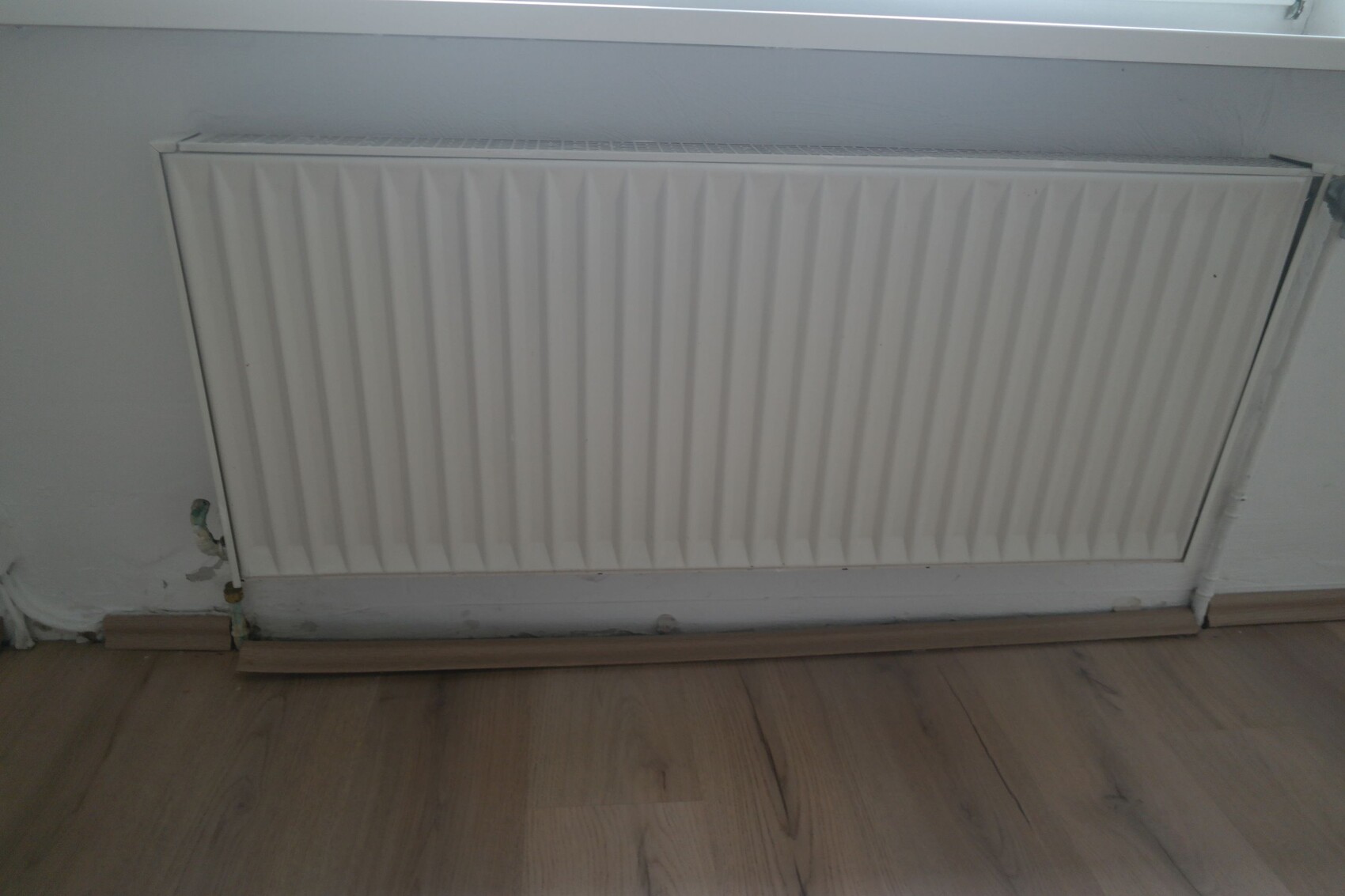 Weißer Heizkörper mit vertikalen Lamellen an der Wand über Holzfußboden.