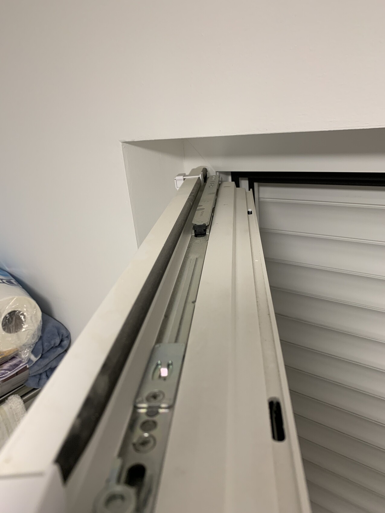 Nahaufnahme eines Rollladenmechanismus mit Führungsprofilen in einer Fensternische.