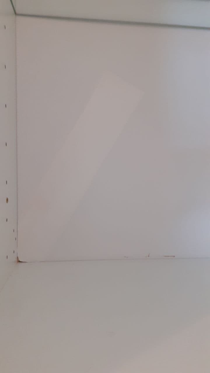 Weiße Innenwand eines Schranks mit Lochreihe am linken Rand; Boden sichtbar.