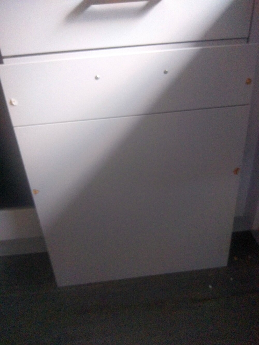 Weißer Schubladenschrank mit drei Schubladen, leicht schräg auf dunklem Boden