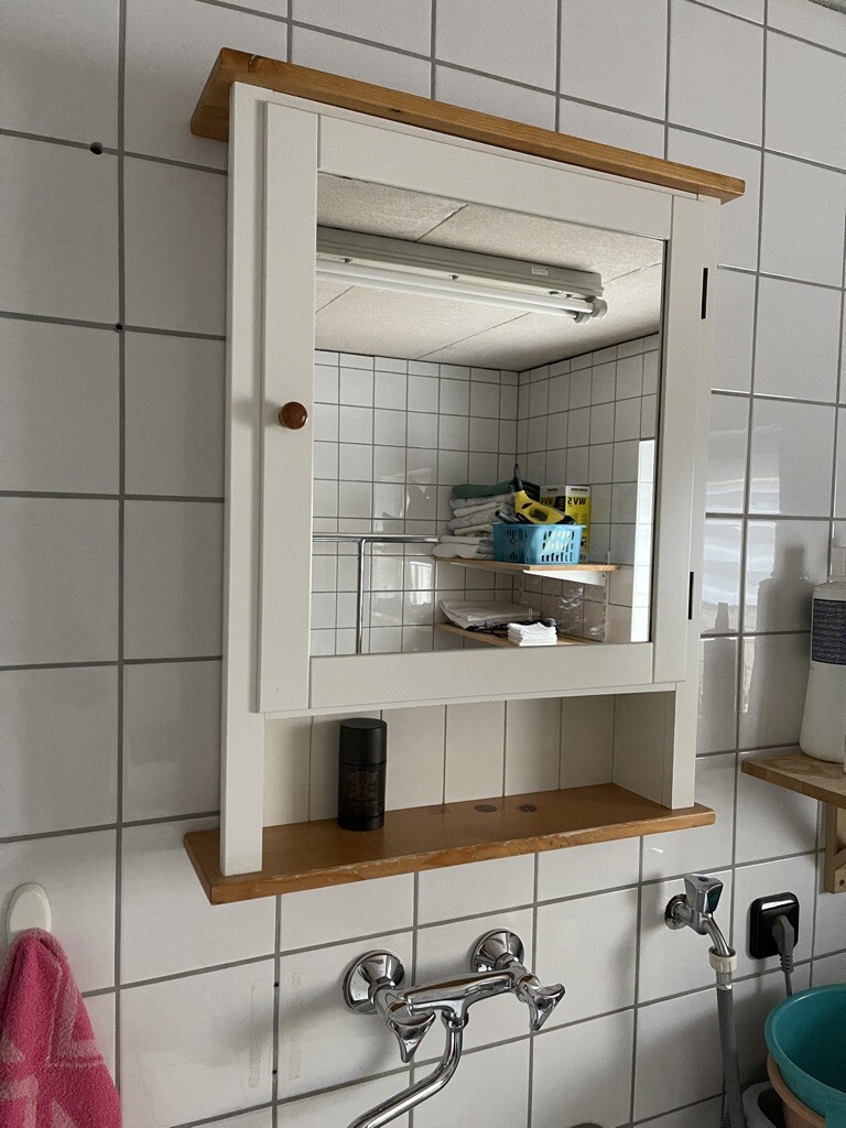Weißer Spiegelschrank mit Holzablage über Waschbecken; Innen Körbe, Handtücher.