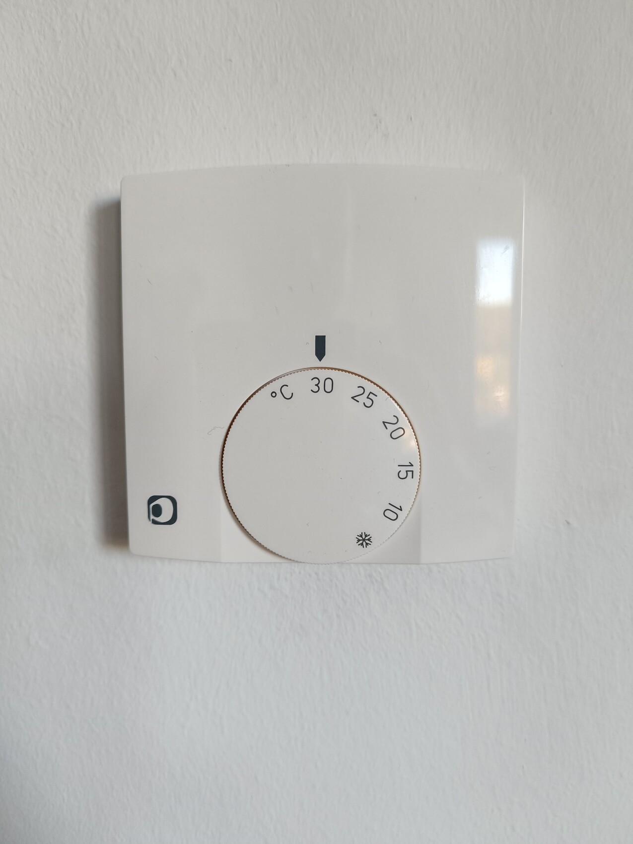 Weißes Wandthermostat mit rundem Drehknopf zur Temperatureinstellung 10–30 °C.