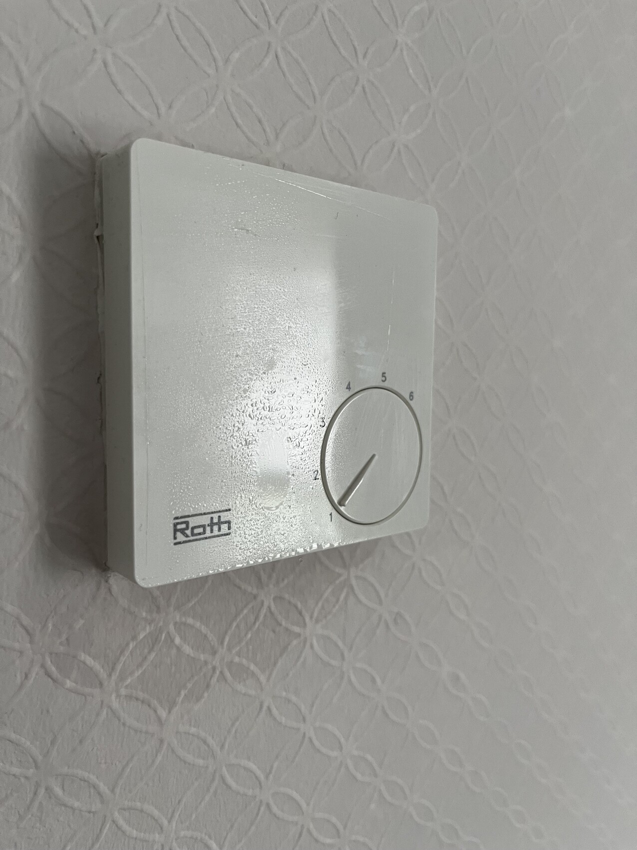 Weißer Wandthermostat mit Rundknopf, Skala 0-6 und Roth-Logo.
