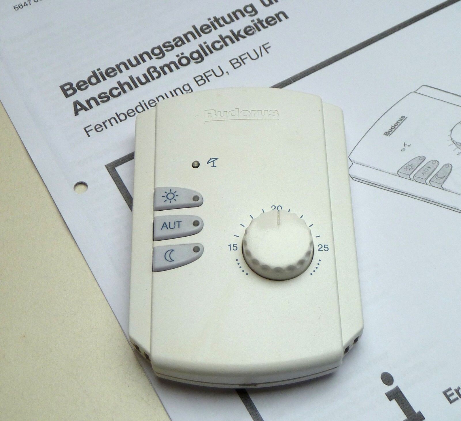Weisser Thermostat mit Drehknopf liegt auf Papier mit Bedienungsanleitung