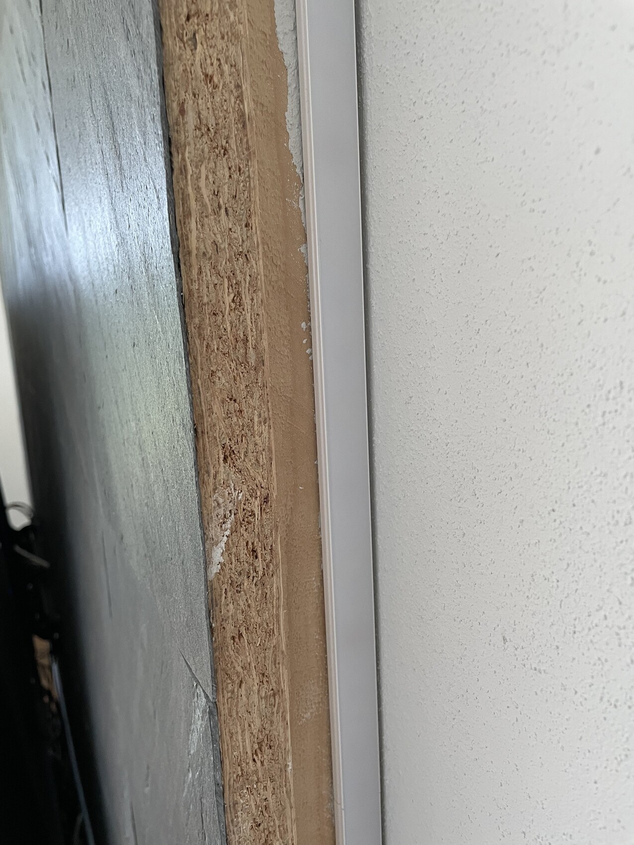 Türrahmen-Spalt: braunes Holz links, weiße Wand rechts, silbernes Dichtungsprofil dazwischen.