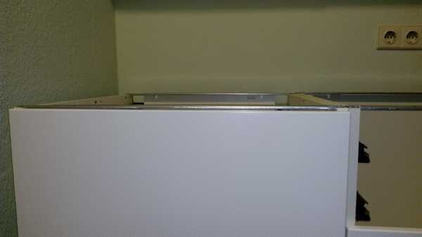 Offene weiße Küchenschublade mit Metallführung; Steckdosen an Wand im Hintergrund.