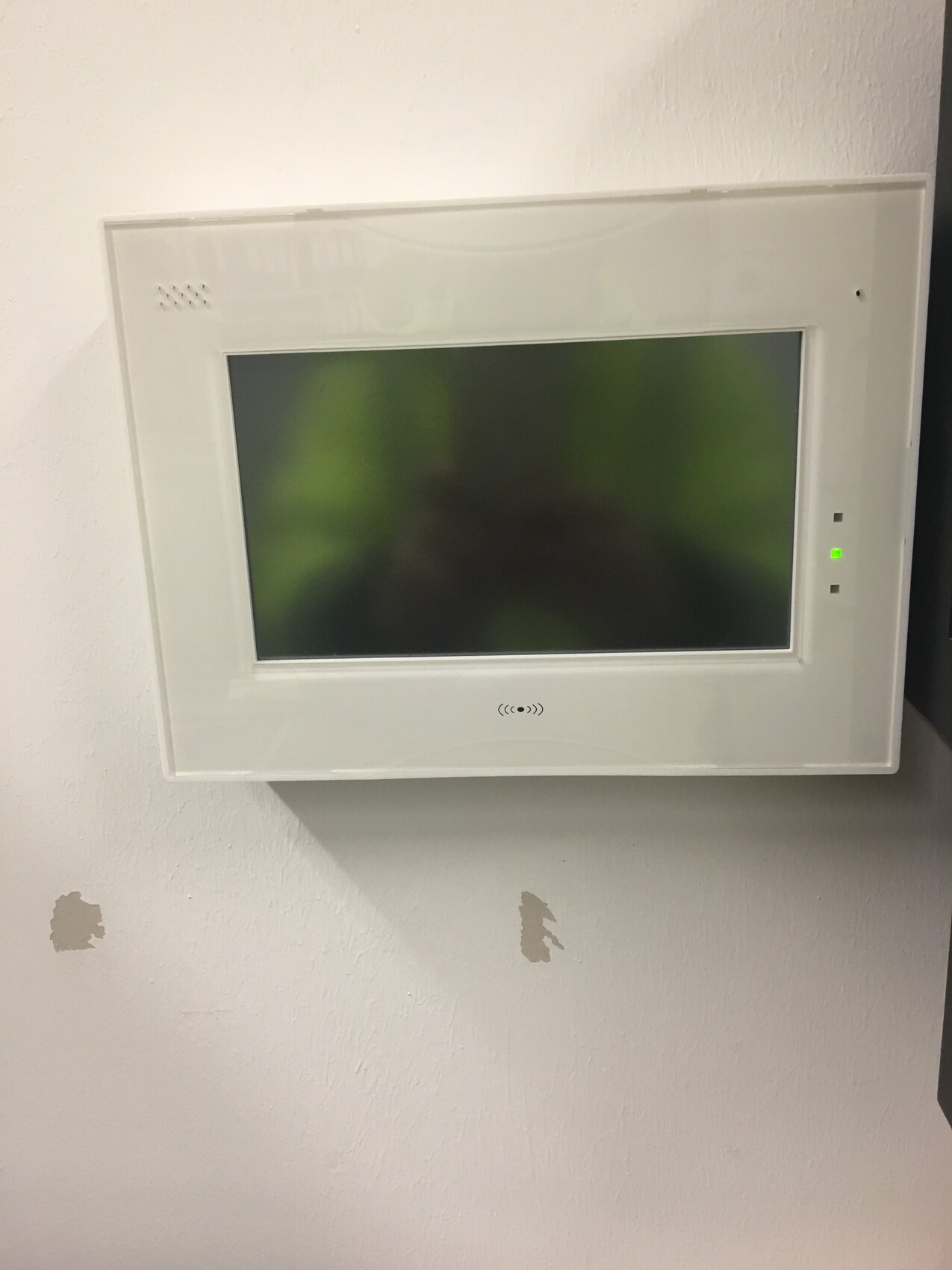 Weißer Wand-Monitor mit großem Display, an der Wand montiert; rechts grüne LED.