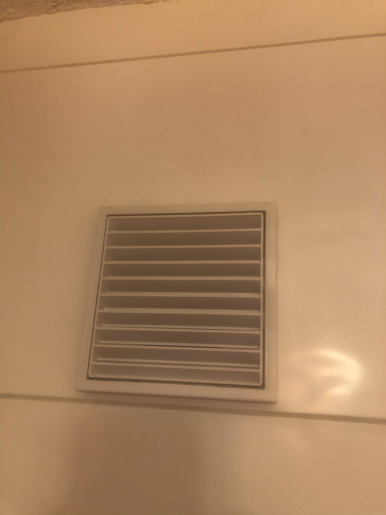 Weiße quadratische Lüftungsabdeckung mit horizontalen Lamellen an einer Wand.